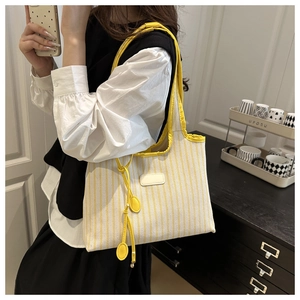 Détail du sac cabas en toile à rayures jaunes et blanches avec bandoulière et étiquette