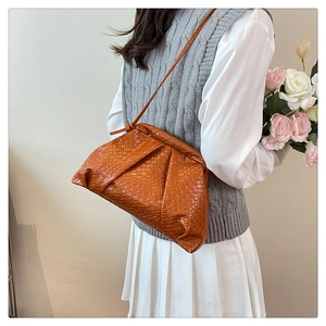 Detail of orange woven cloud bag with leather texture worn cross-body by a model