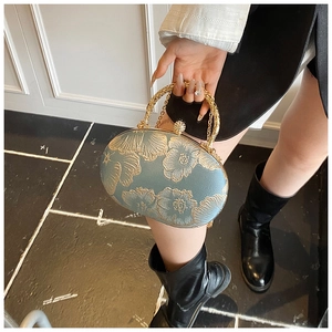 Top view of a light blue embroidered evening bag with golden floral patterns and ring handle