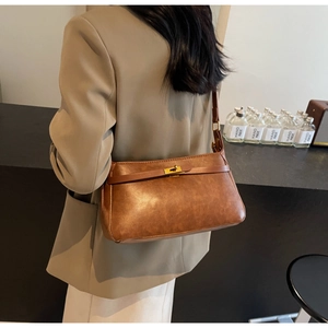 Dettaglio di una borsa baguette vintage marrone con fibbia dorata su una spalla