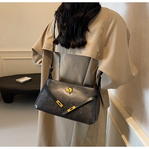 Dettaglio della borsa vintage in pelle nera con fibbia dorata su modella in trench