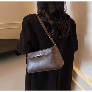 Borsa baguette vintage in pelle marrone scuro portata a spalla su un cappotto nero