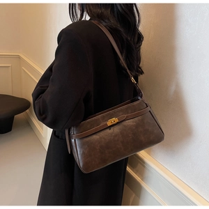Dettaglio della borsa a tracolla vintage marrone scuro con fibbia dorata su cappotto nero