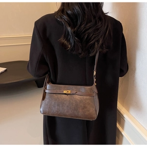 Dettaglio borsa a spalla retrò in pelle marrone con chiusura dorata su cappotto nero