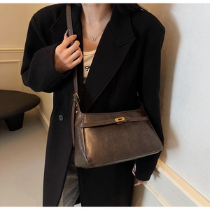 Dettaglio borsa vintage in pelle marrone con chiusura dorata su modella con blazer nero