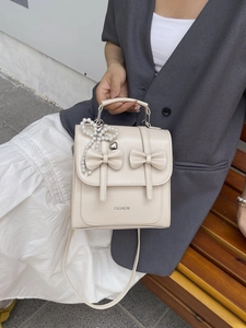 Petit sac à dos beige chic avec nœuds et charm en perles porté avec une tenue urbaine