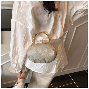 Detailed view of qipao style evening clutch with golden floral embroidery and ring handle