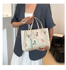 Detail of white tote bag featuring koi fish patterns and green tassel on a shoulder strap
