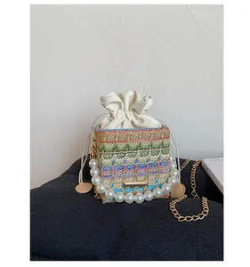 Close-up of a colorful woven bucket bag with pearl handle and gold chain strap detail