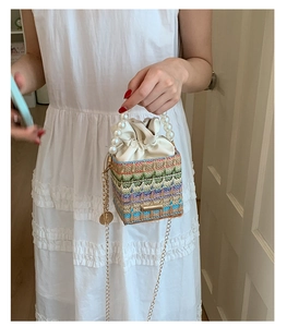 Detail of colorful woven straw bucket bag with pearl handle and golden chain strap