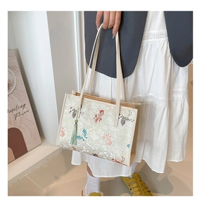 Gros plan détaillé des motifs de papillons et carpes koi brodés sur un sac cabas crème