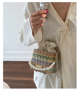 Detail of woven bucket bag featuring pearl handle and gold chain strap on model