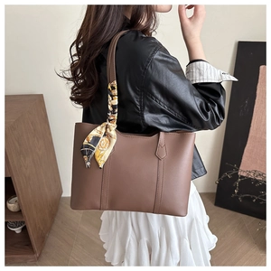 Detail of a brown leather tote bag with vertical stitching and decorative scarf