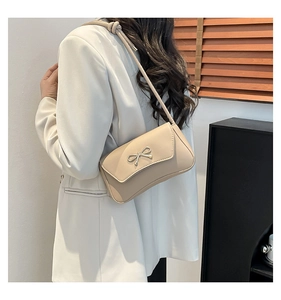 Dettaglio della borsa sottobraccio beige con fibbia a fiocco metallico su blazer bianco