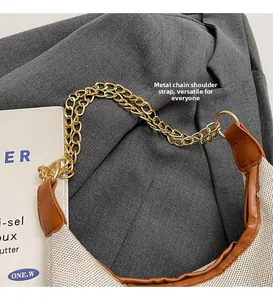 Dettaglio della tracolla a catena dorata su borsa tote in tela beige e pelle marrone