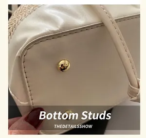 Détail du fond du sac en cuir crème avec des pieds de protection dorés et coutures précises
