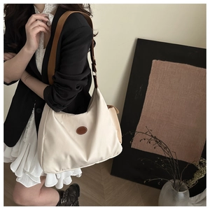 Detail of cream nylon tote bag featuring a brown leather fashion patch and wide strap