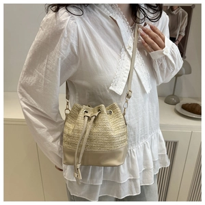 Détail du sac seau en paille avec garniture en cuir beige et bandoulière réglable
