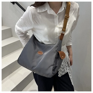Detail of grey nylon crossbody bag with fashion patch, brown strap and gold metal buckle