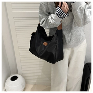Detail of black nylon tote bag with brown leather logo patch and metal buckle on shoulder strap