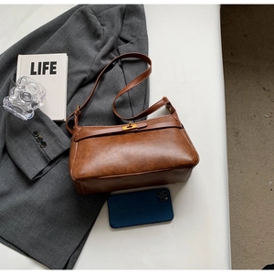 Dettaglio di una borsa a tracolla vintage in pelle marrone con chiusura dorata su tessuto grigio