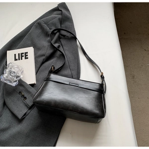 Dettaglio della borsa sottobraccio minimalista in pelle nera con tracolla e fibbia retrò