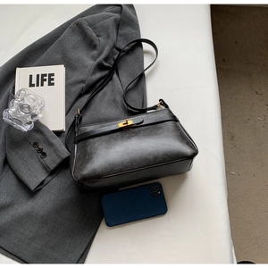 Dettaglio di una borsa vintage in pelle nera opaca con chiusura a rotazione dorata su abito