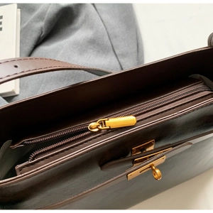 Dettaglio borsa in pelle marrone con chiusura a rotazione dorata e doppi scomparti con zip