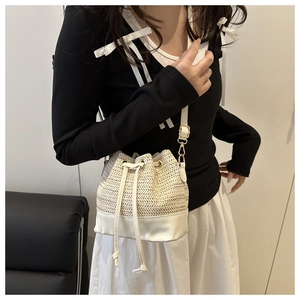 Détail du sac seau en paille tissée avec garniture en cuir blanc et cordon sur modèle