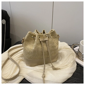Détail du sac seau en paille beige montrant la texture tressée et la finition en similicuir