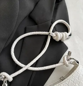 Detail of white woven shoulder strap with knot design and silver hardware on handbag