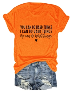 Flat lay of an orange crew neck t-shirt with inspirational text and ripped denim shorts