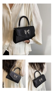 Detail of black glitter crossbody bag featuring silver metal bow and chain strap