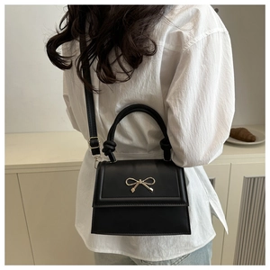 Borsa a mano nera minimalista con chiusura a fiocco dorato indossata da modella elegante
