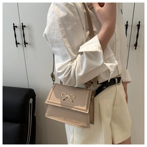 Dettaglio borsa a tracolla beige con fibbia a fiocco dorata su camicia di lino
