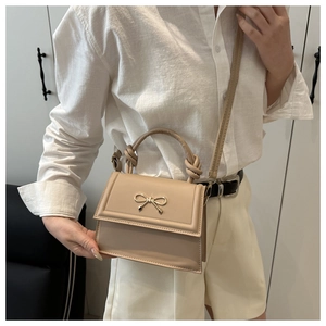 Dettaglio di un'elegante borsa beige con fiocco dorato indossata da una modella
