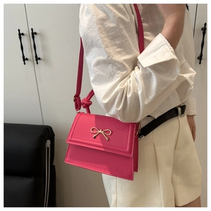 Dettaglio della mini borsa a patta fucsia con fiocco in metallo dorato e manico superiore