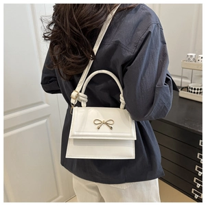Borsa a mano bianca con fiocco indossata a tracolla da una modella con camicia blu