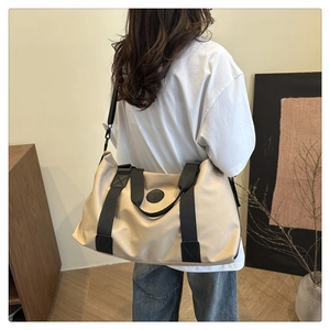 Detailed view of the beige canvas travel bag with black shoulder strap worn by a model