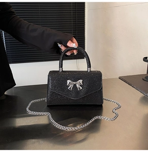 Detail of black sequin handbag featuring a silver metal bow buckle and chain strap