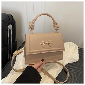 Dettaglio borsa a trapezio beige con fiocco dorato e manico annodato elegante