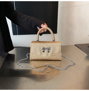 Detail of glittery gold square bag with silver metal bow and shiny chain strap