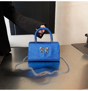 Close-up of shiny blue glitter handbag with silver metal bow and chain strap detail