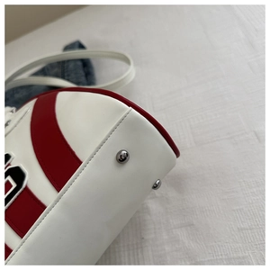 Detalle de la base del bolso con remaches metálicos plateados y paneles de cuero rojo