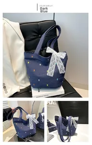 Detalle del bolso tote denim azul oscuro con bordados florales y lazo de encaje blanco