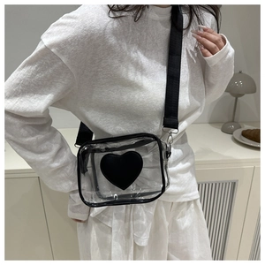 Close-up of transparent PVC crossbody bag featuring a black heart patch and wide strap