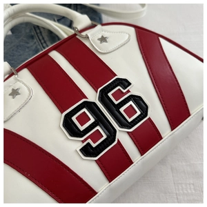 Detalle de bolso Boston blanco con rayas rojas, parche número 96 y remaches de estrella