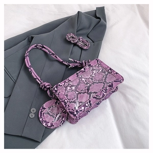 Détail du sac bandoulière violet à motif serpent avec breloque assortie sur fond gris