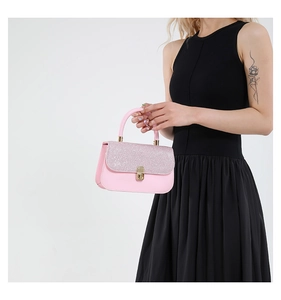 Detail of pink glitter flap handbag with gold metal lock held by a model in a black dress