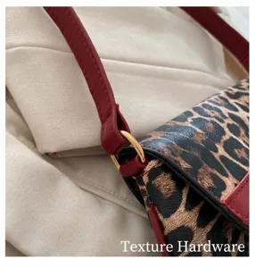 Détail du sac léopard montrant les ferrures dorées et le connecteur de bandoulière rouge